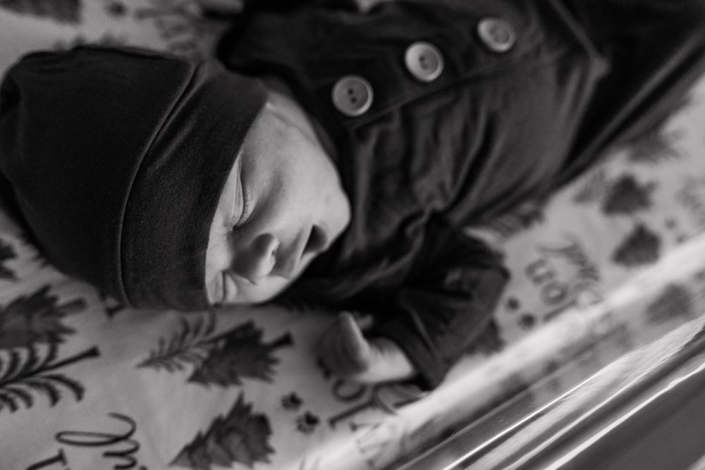 Baby bundled in black winter coat lying on patterned fabric.