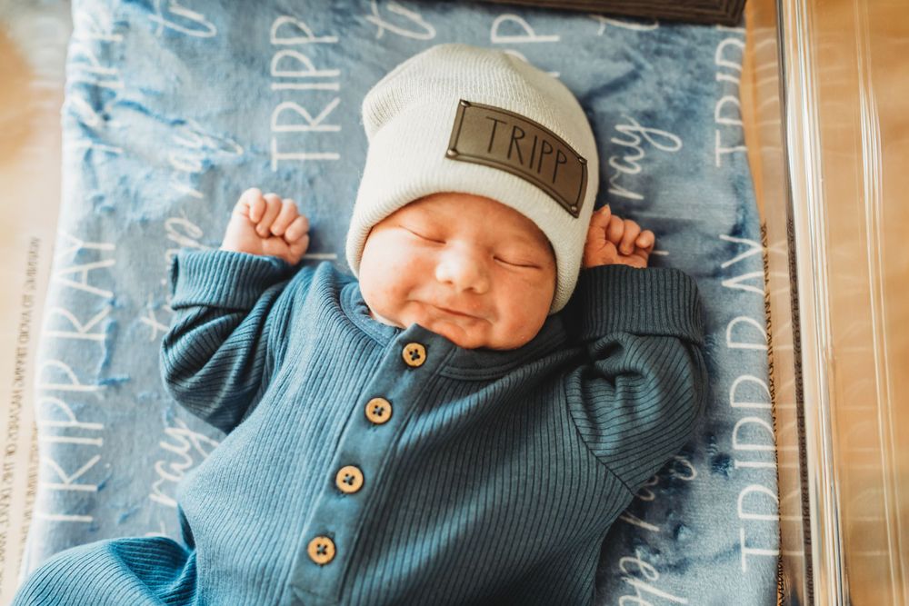 Sleeping newborn in blue knit outfit and beanie on patterned background.