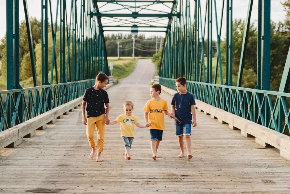 Family walking along green metal bridge while holding hands during sunset.