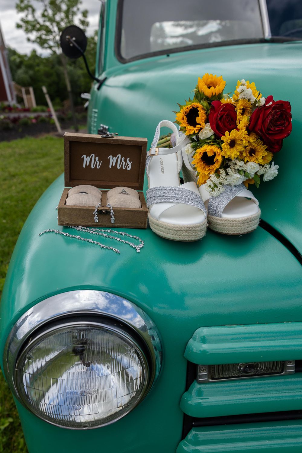 Wedding details arranged on a vintage turquoise truck including sunflowers, roses, and bridal shoes.