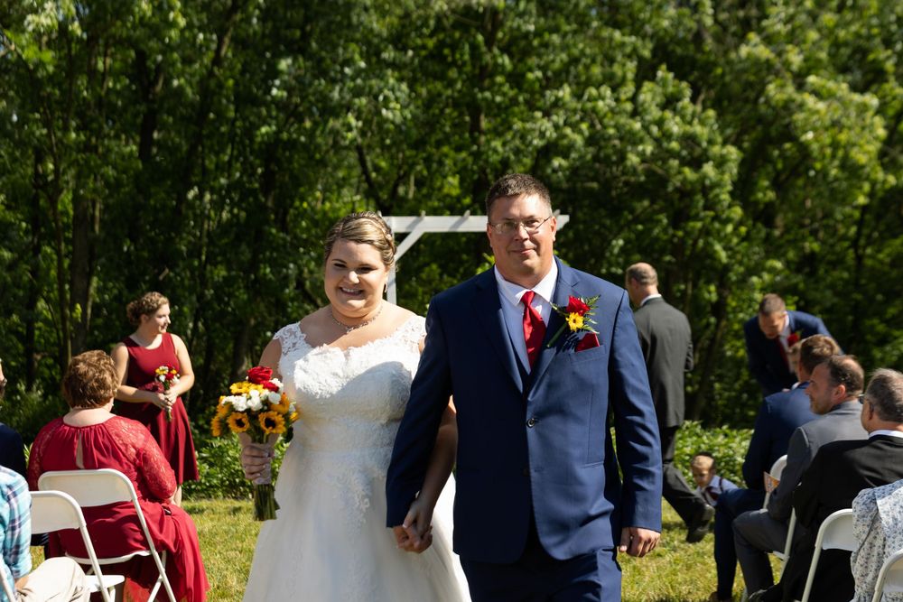 A newly married couple walks down the aisle at their outdoor summer wedding.