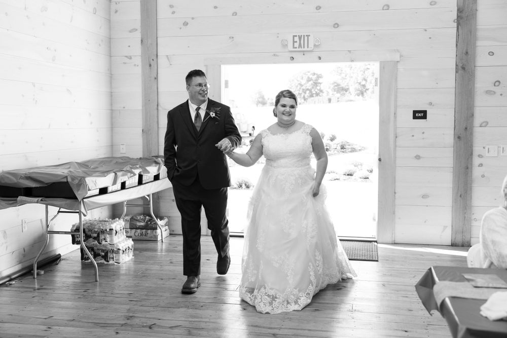 A black and white photo of a couple making their entrance into a rustic venue.
