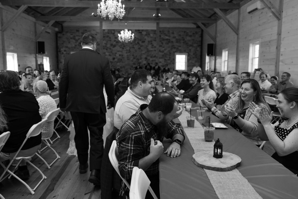 Reception guests seated at long tables in a rustic venue with chandeliers and stone walls.