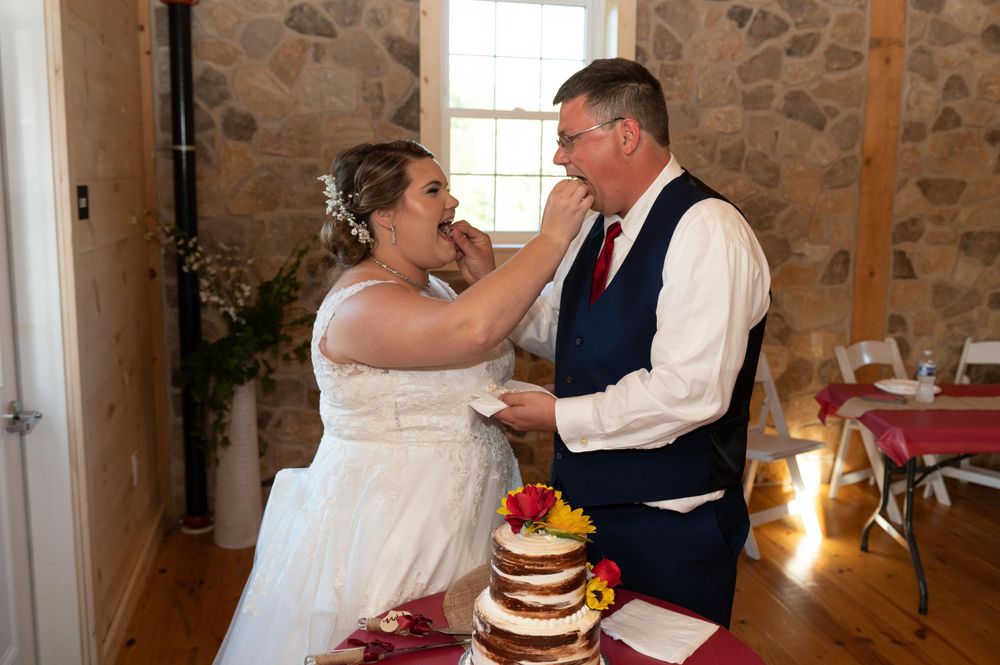 A couple celebrating their wedding day with a sweet moment by their rustic tiered cake.