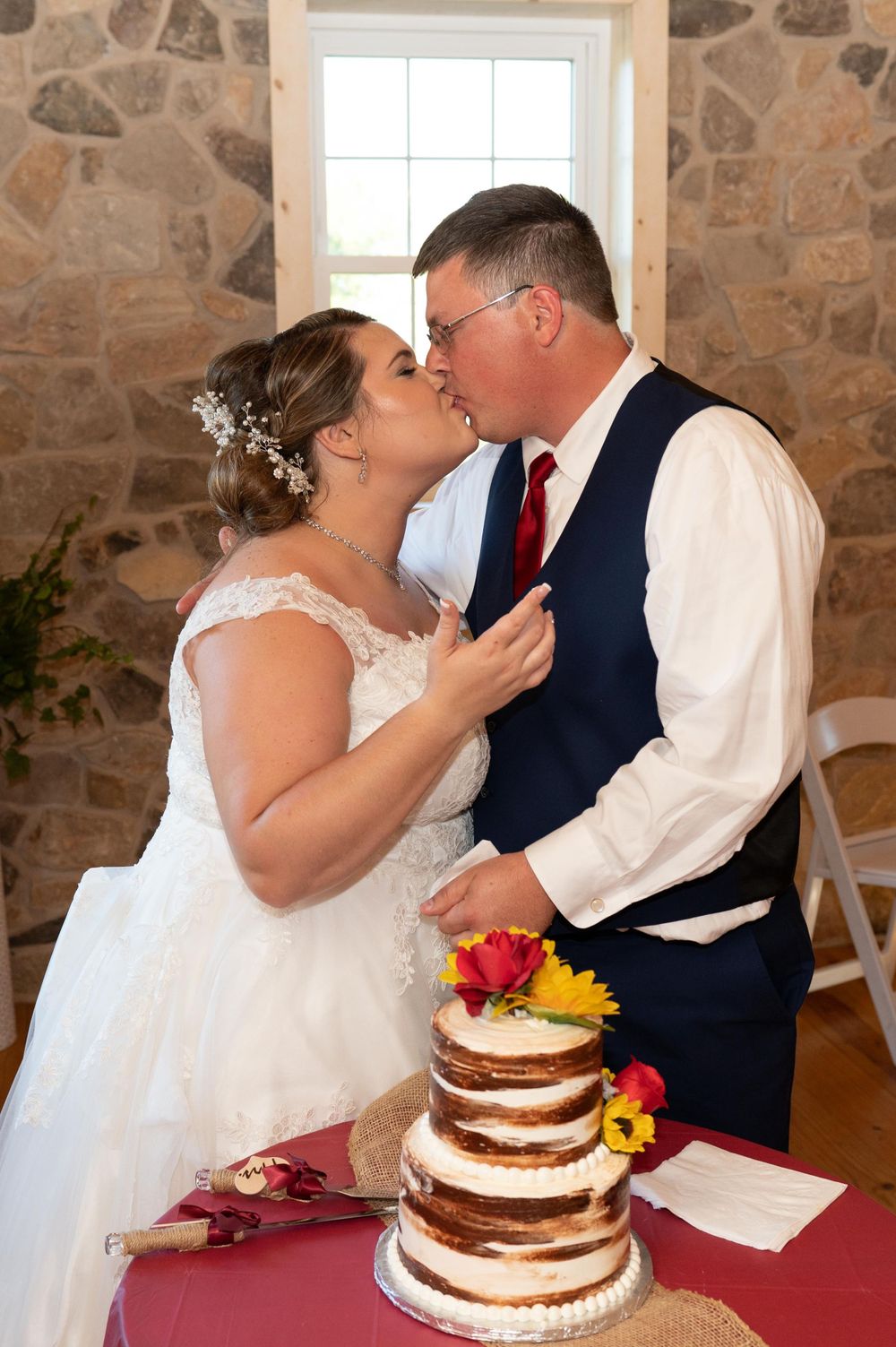 A couple sharing a romantic moment while cutting their tiered naked wedding cake.