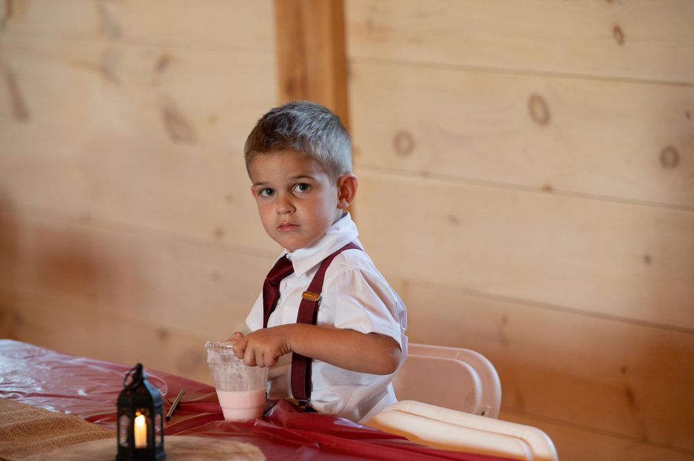 Young guest in white shirt and red tie sitting at wedding reception table with beverage.