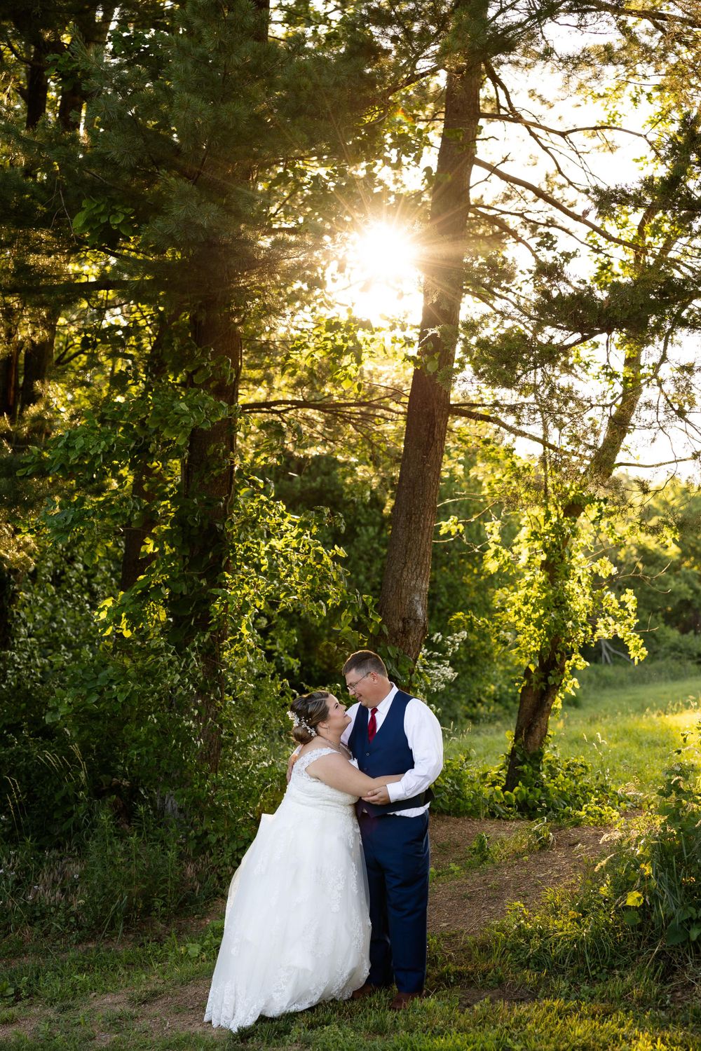 Newlyweds embracing on a forest path with golden sunlight streaming through the trees.