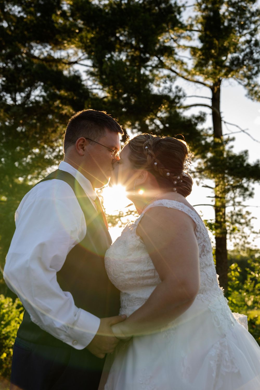 Silhouetted couple in wedding attire embracing with sunset backlight through trees.