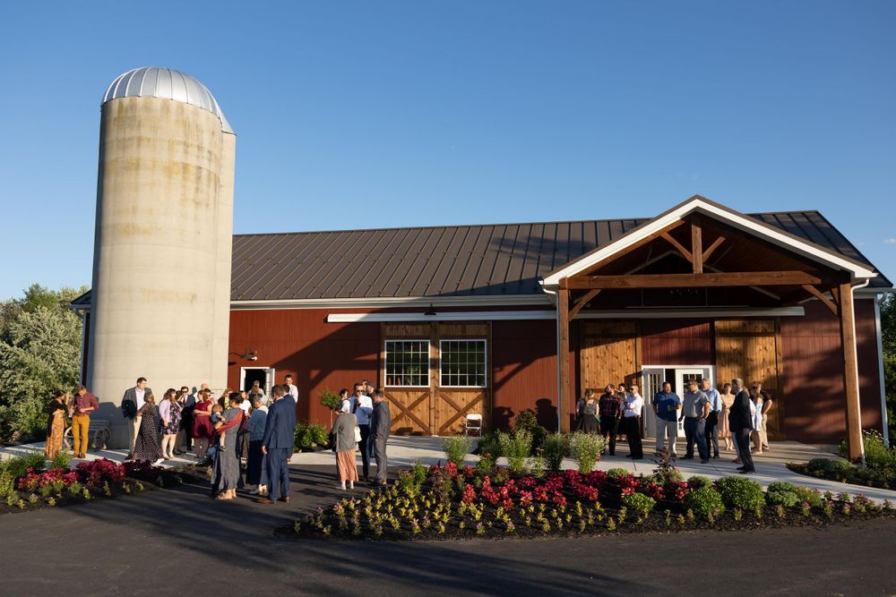 Rustic barn wedding venue with silo and gathering of guests outside at dusk.