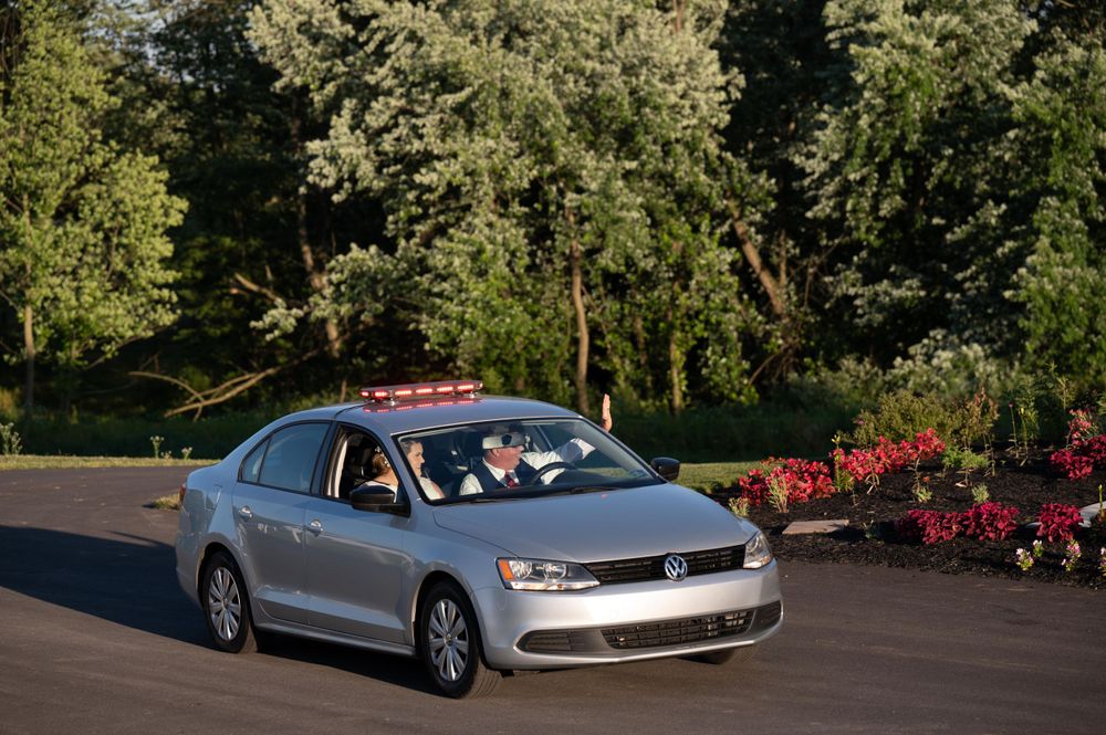 Silver Volkswagen Jetta driving past blooming flowers in a garden setting.
