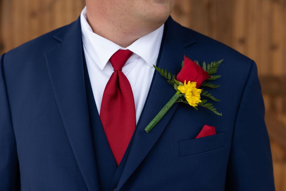 A close-up of a navy suit with red tie and colorful boutonniere featuring yellow and red flowers.