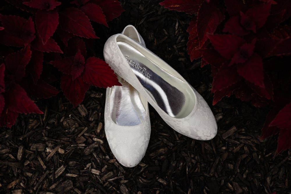 White lace wedding flats displayed on dark ground with dramatic lighting.