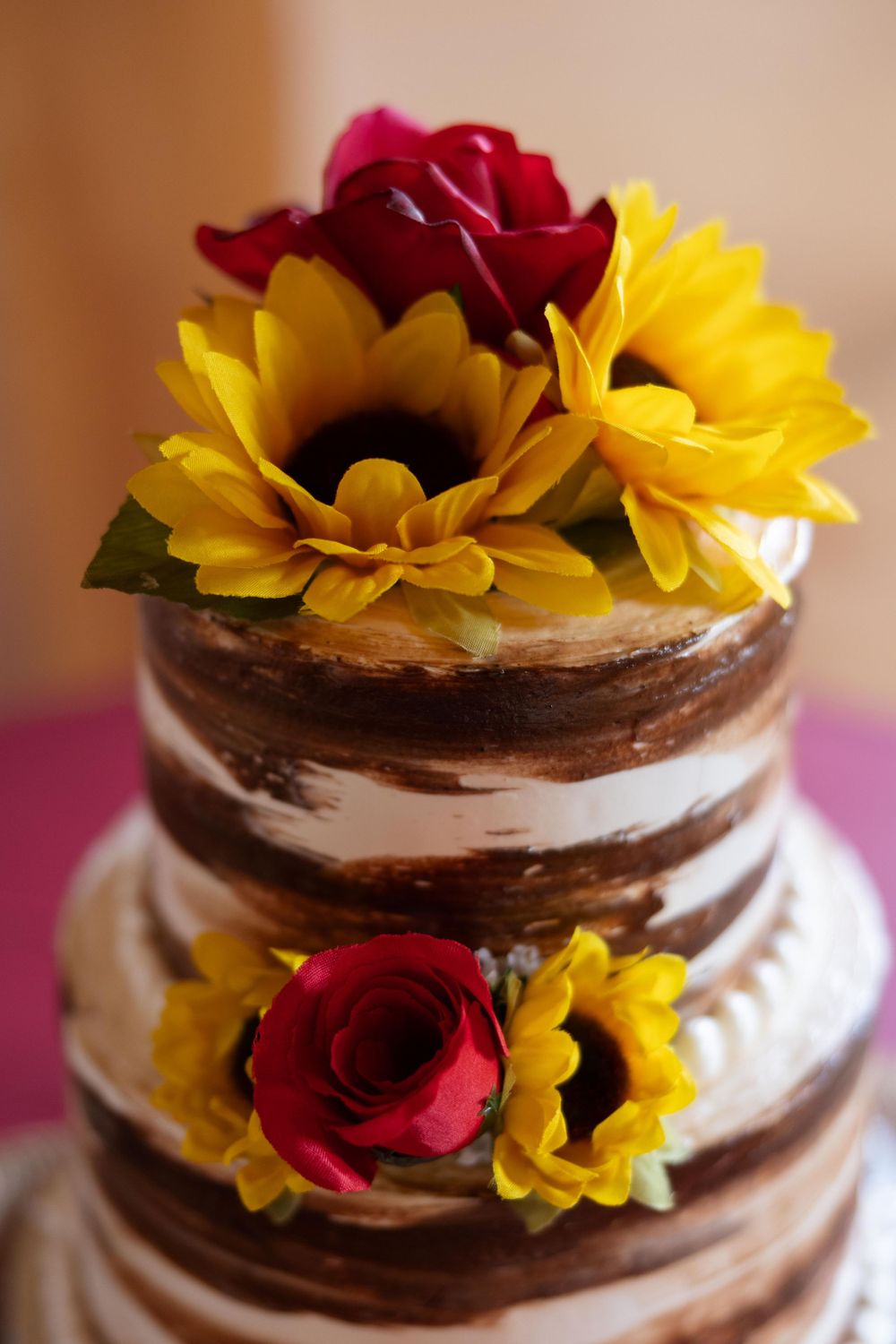 Three-tiered chocolate naked cake decorated with red roses and yellow sunflowers.