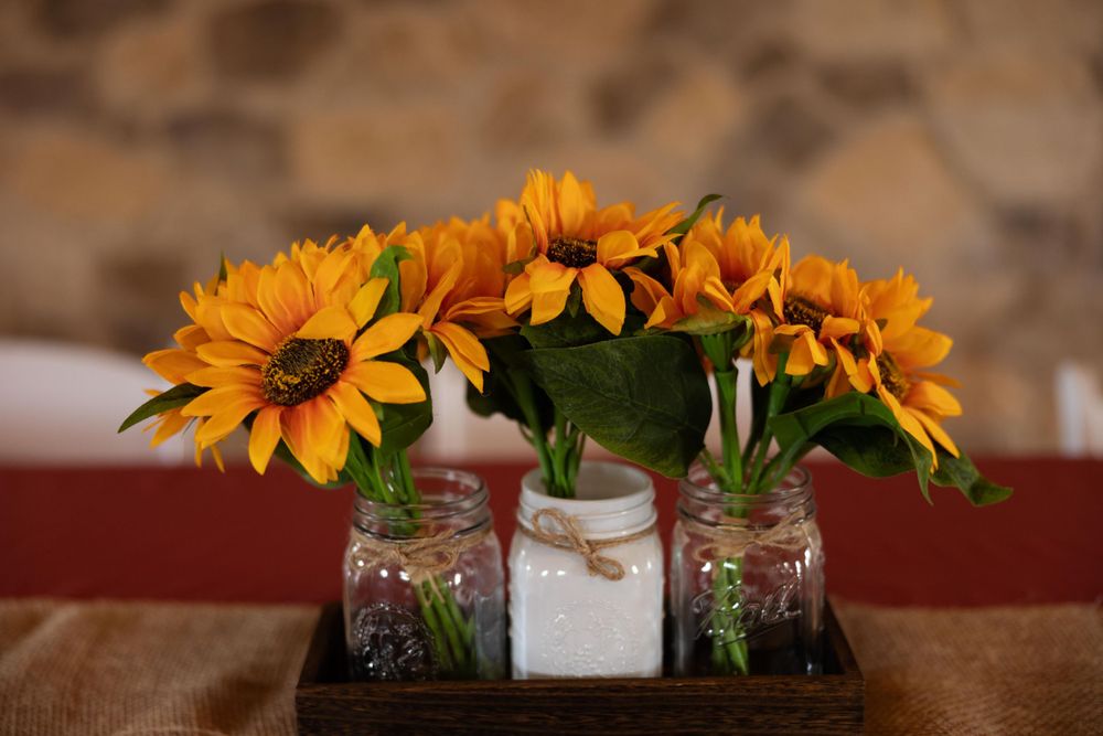 Three mason jars filled with sunflowers arranged on a wooden tray.