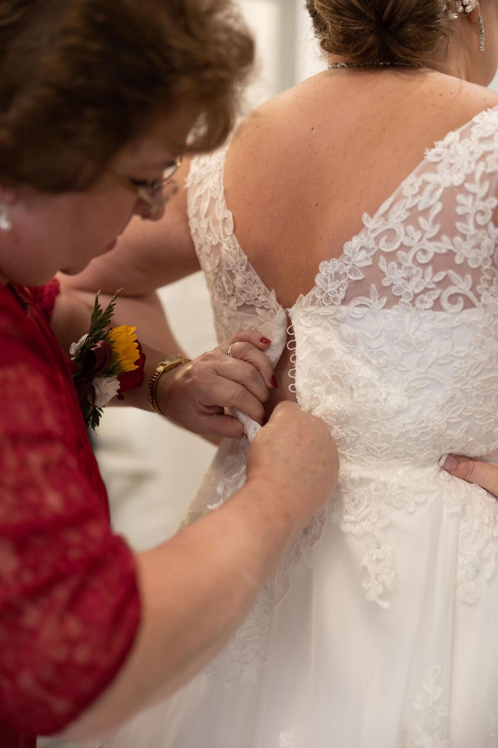 Close-up of buttons being fastened on a white lace wedding dress.