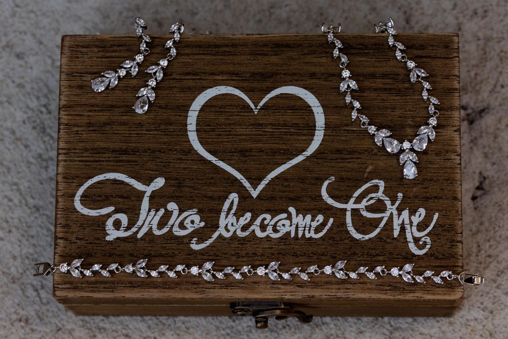 Wooden wedding sign with cursive text 'Two Become One' decorated with crystal jewelry.
