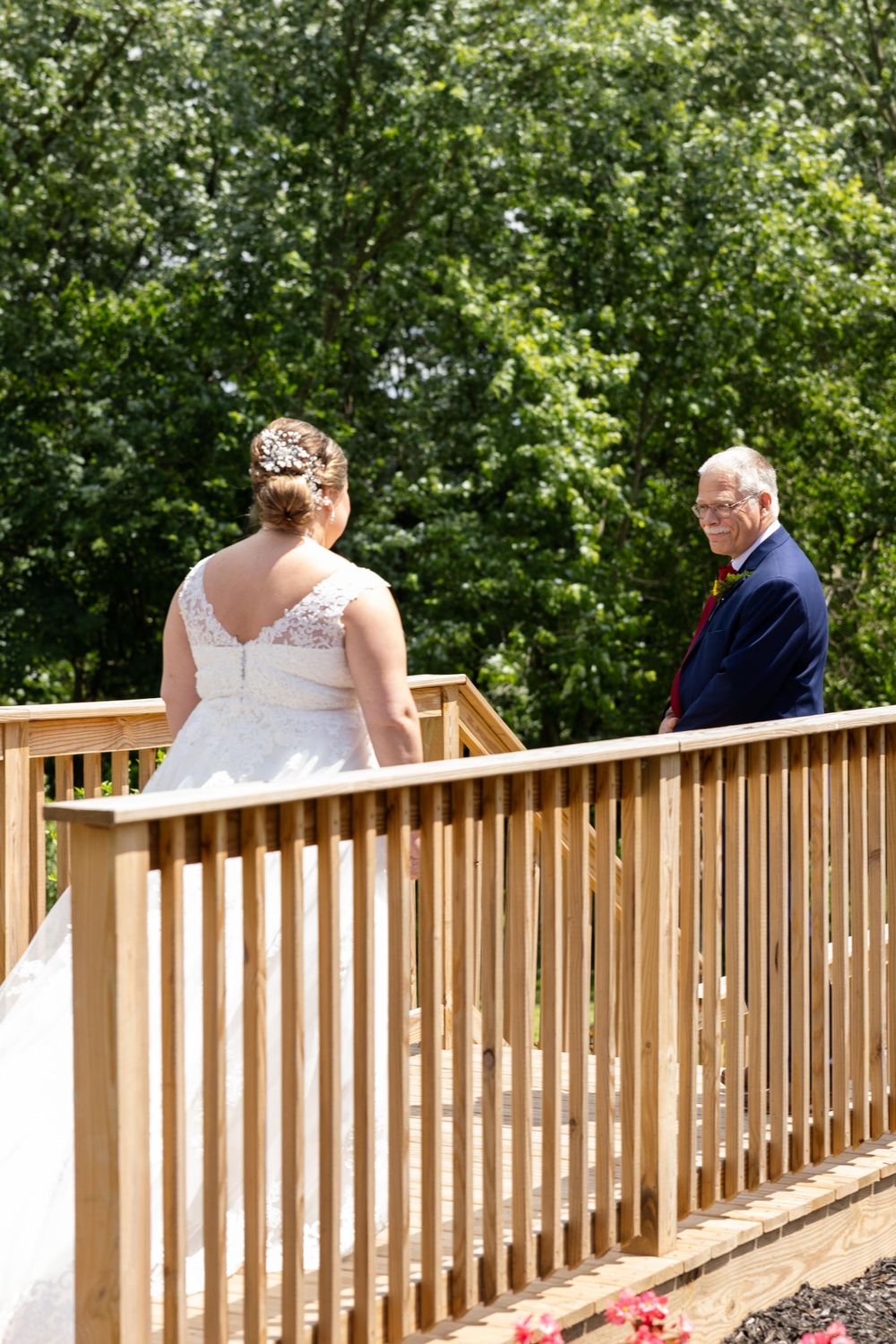 A white wedding dress with lace details stands out against the natural greenery on a wooden deck.