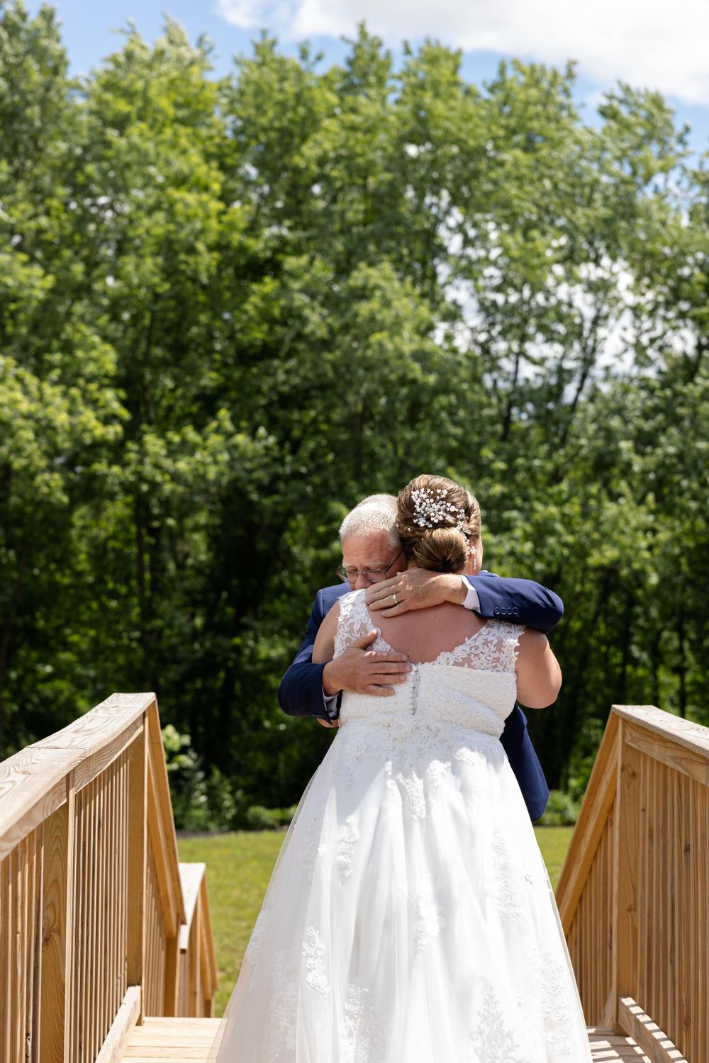 An emotional embrace is shared between two people on a wooden bridge surrounded by trees.