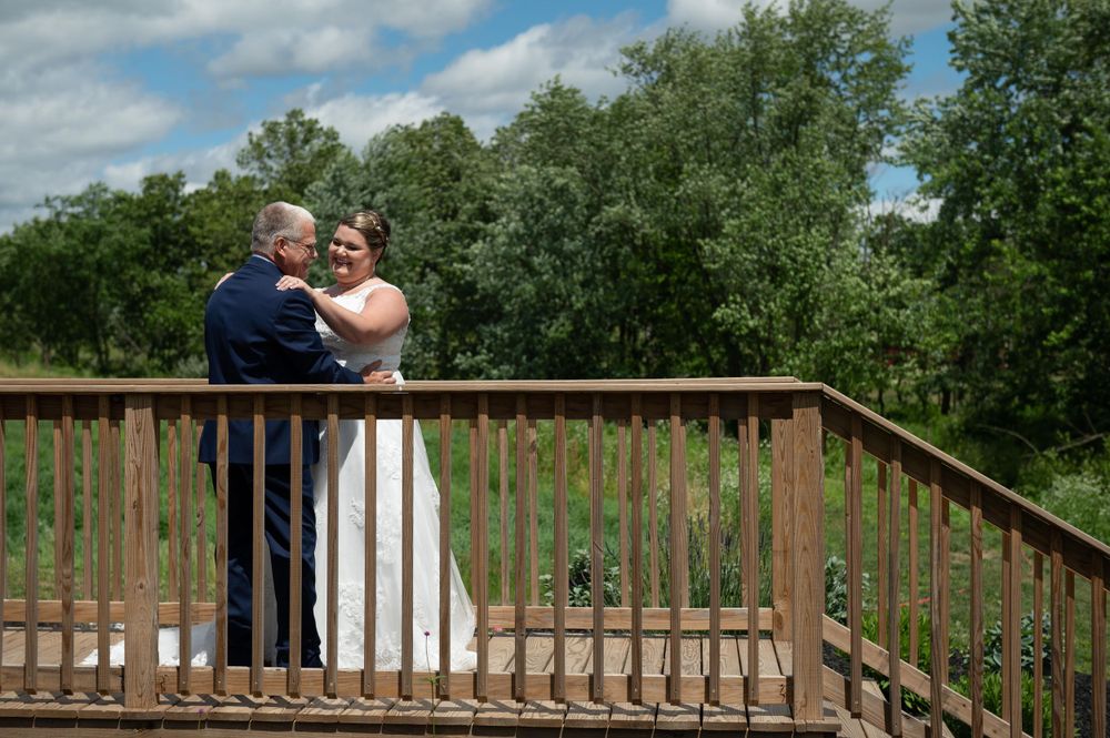 A loving embrace is captured on a wooden deck with trees and blue sky in the background.