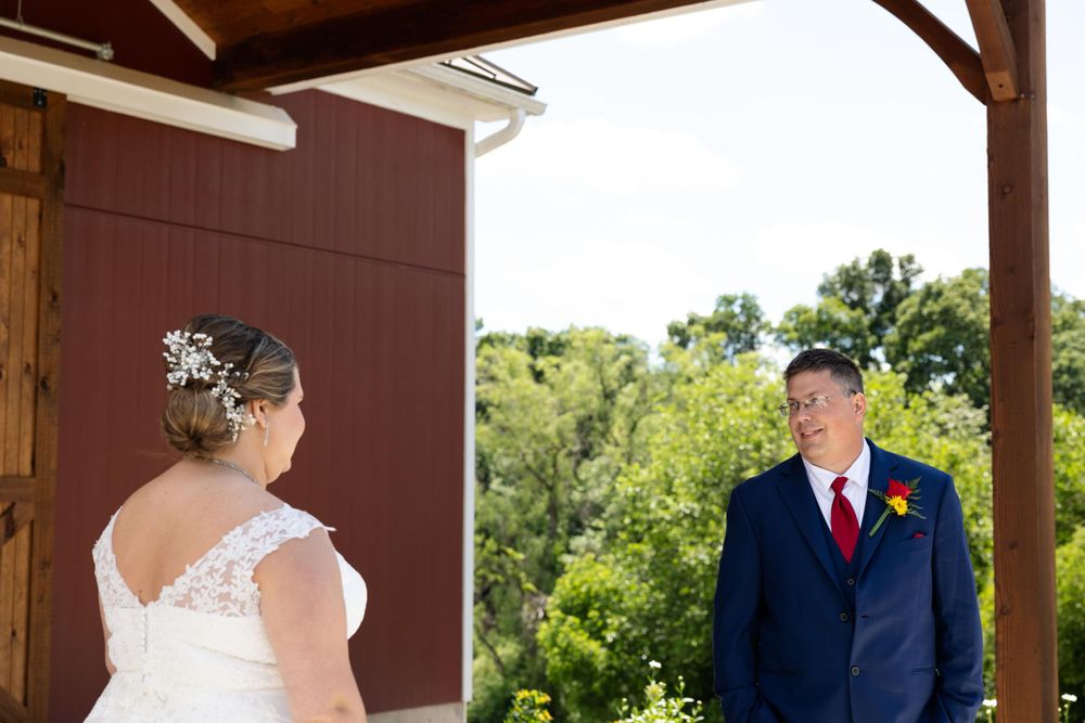 A beautiful rustic first look scene with a red barn wall and natural outdoor backdrop.
