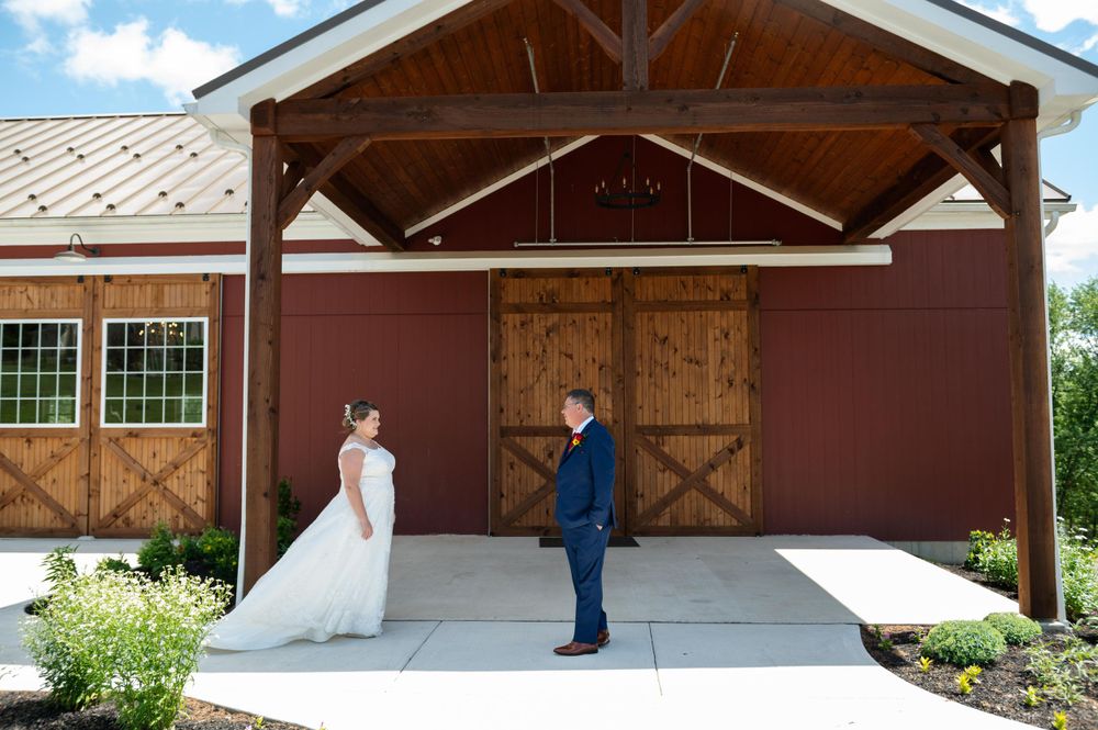 A wedding first look takes place outside a rustic barn with wooden doors and exposed beams.