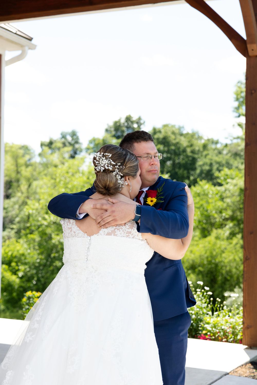 A romantic wedding moment captured under a wooden pavilion with lush greenery in the background.