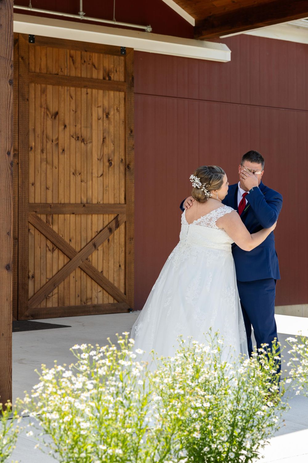 A couple shares their first dance in front of a rustic barn door with delicate wildflowers in the foreground.