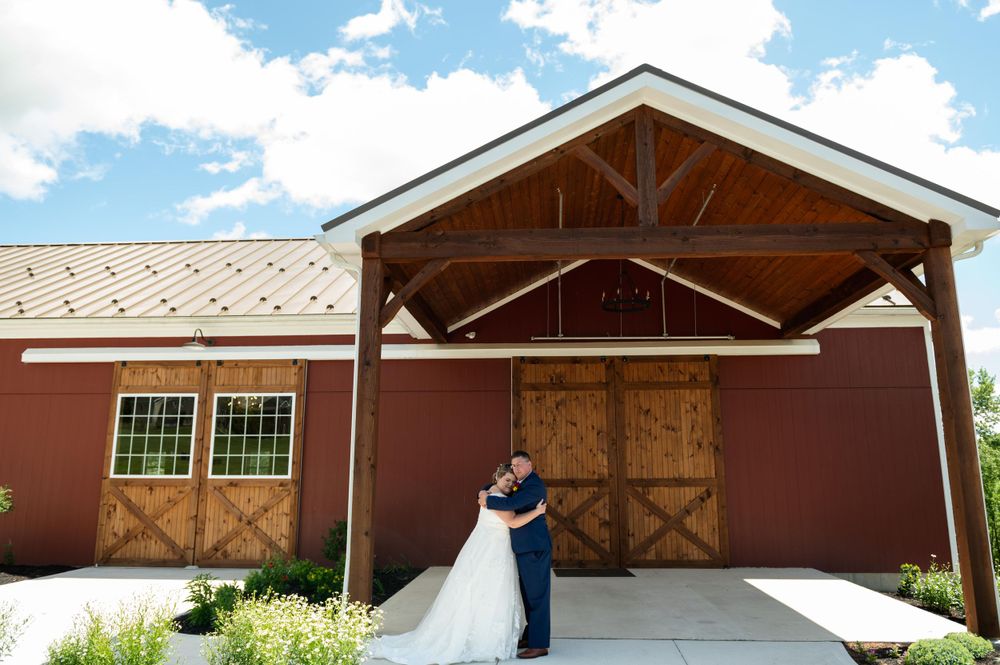 Wedding couple embracing in front of a red barn with wooden doors under a covered entrance.