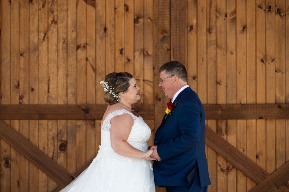 Intimate wedding moment captured against rustic wooden barn doors with exposed beams.