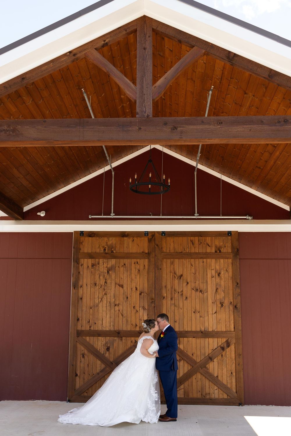 Elegant wedding portrait against a barn facade with vaulted wooden ceiling and rustic doors.