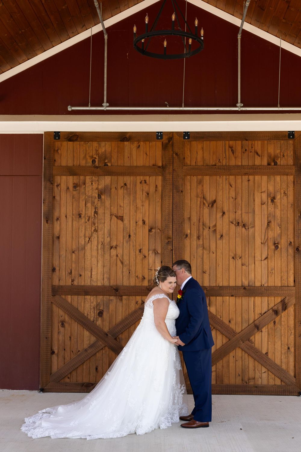 Romantic wedding photo against wooden barn doors with vaulted ceiling and chandelier.
