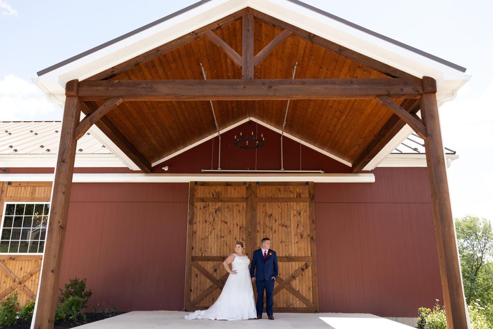 Rustic barn wedding portrait under wooden beams and against large barn doors.