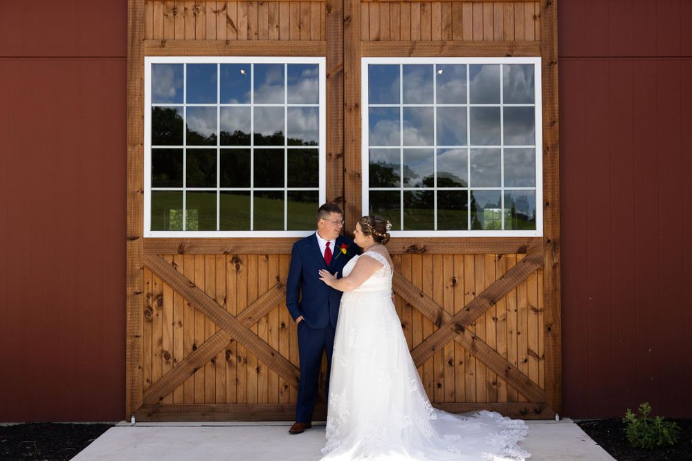 Wedding couple stands together in front of rustic wooden barn doors and windows.