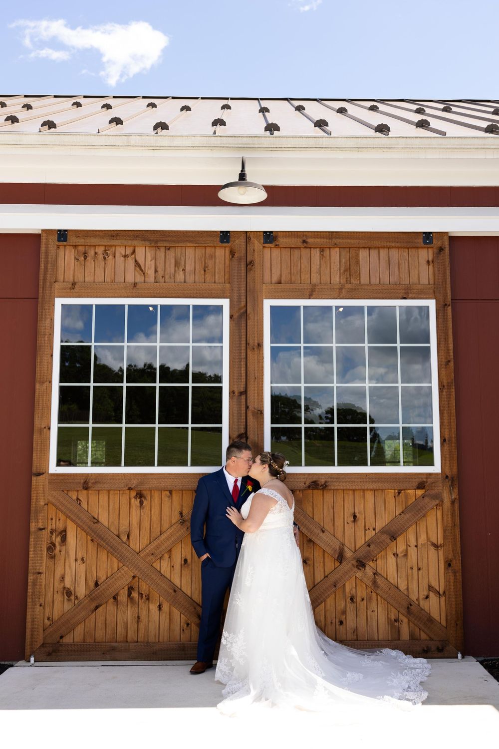 Wedding couple poses against wooden barn doors with reflective windows under metal roofing.