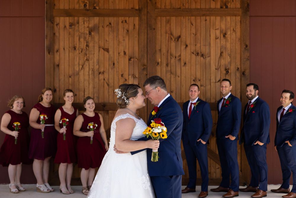 Wedding party lines up against wooden barn door with bridesmaids in burgundy and groomsmen in navy.
