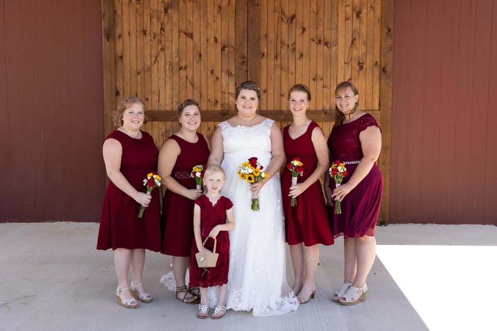 Bridal party in burgundy dresses poses together holding sunflower bouquets.