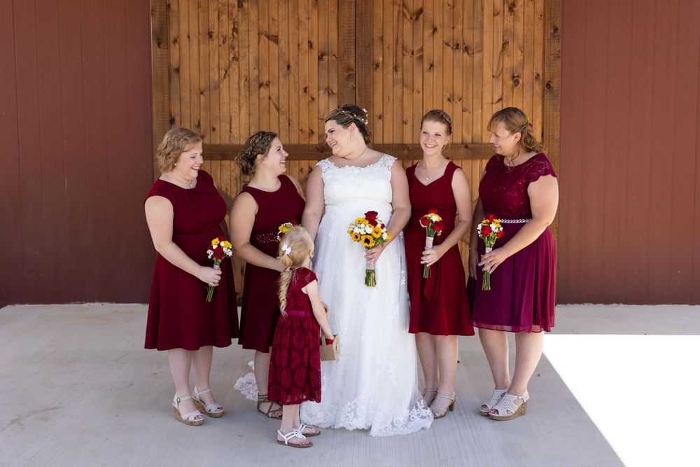 Bridesmaids in burgundy dresses gather around bride holding yellow sunflower bouquets.