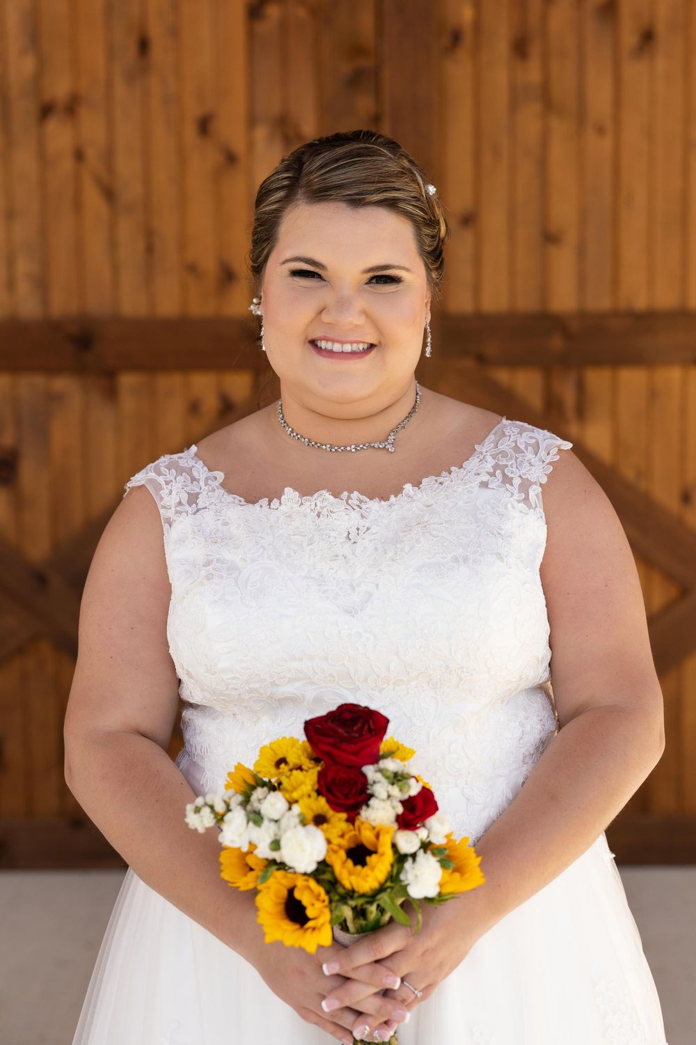 A bridal portrait showcasing a white lace wedding dress and colorful bouquet against wooden barn walls.
