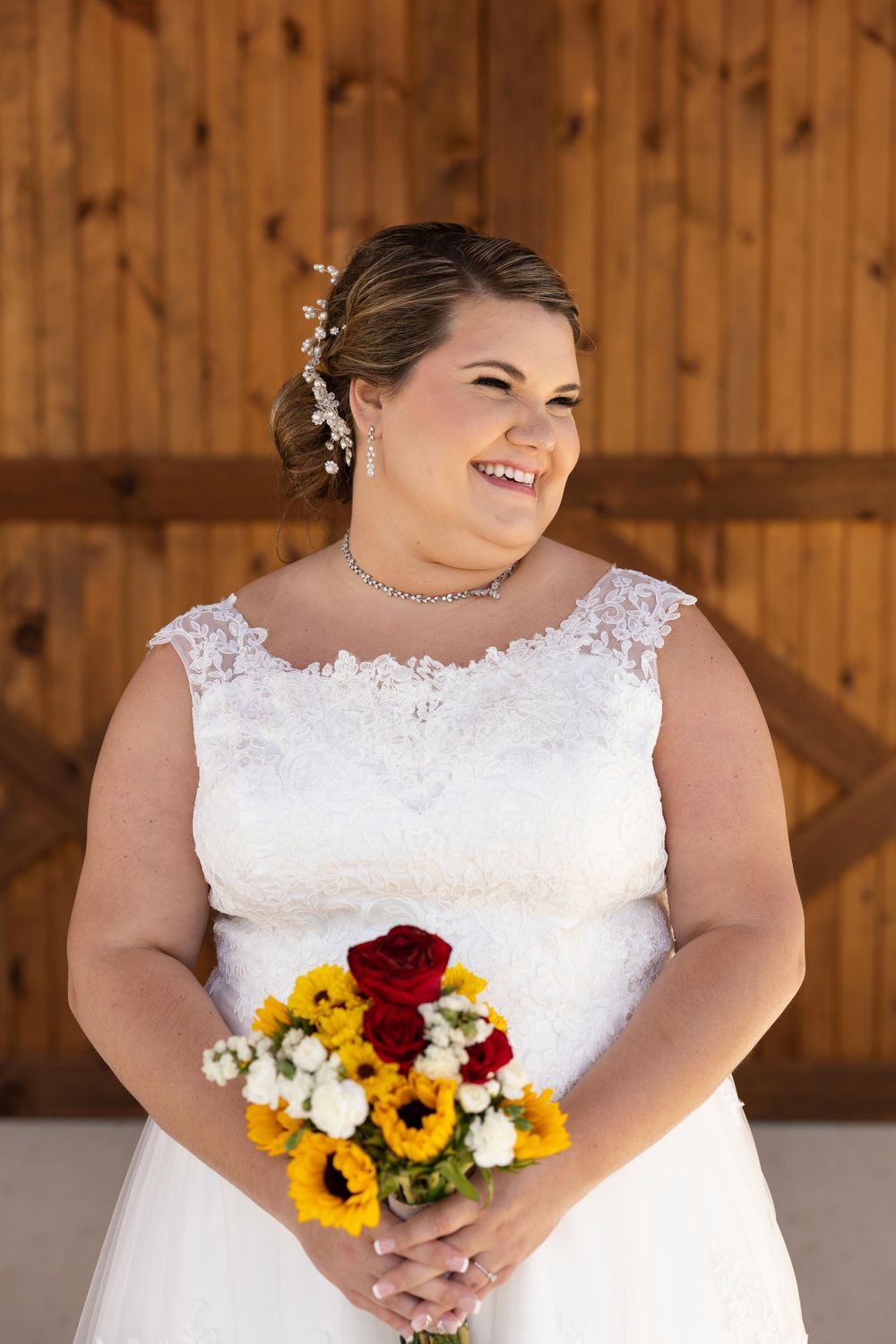 A joyful bridal portrait featuring a white lace dress and sunflower bouquet against rustic wood paneling.