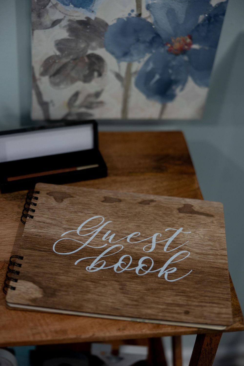Rustic wooden guest book on table with watercolor art hanging in background.