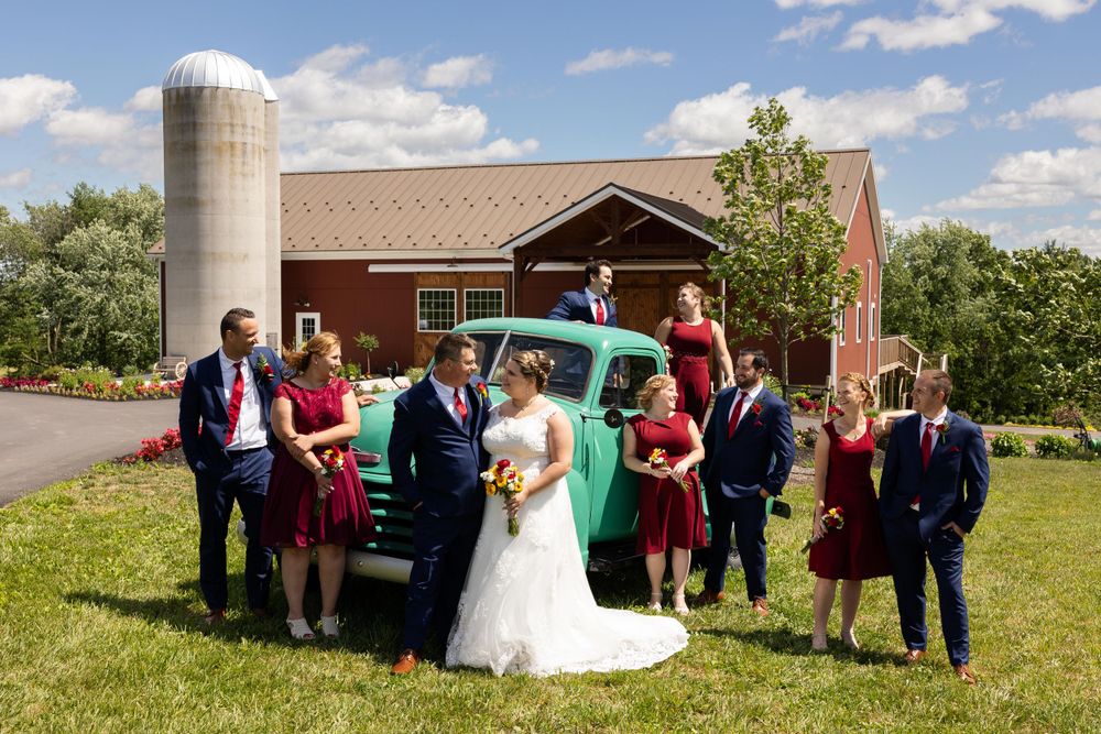 Wedding party poses by vintage mint green truck in front of red barn with silo.