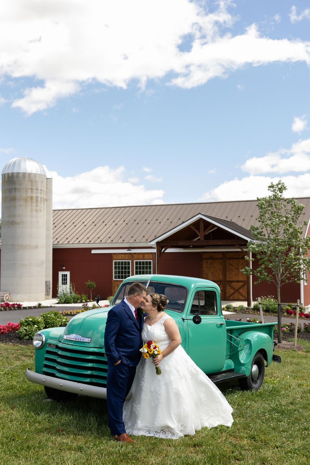 Romantic wedding couple poses with vintage mint green Chevrolet pickup truck at rustic barn venue.