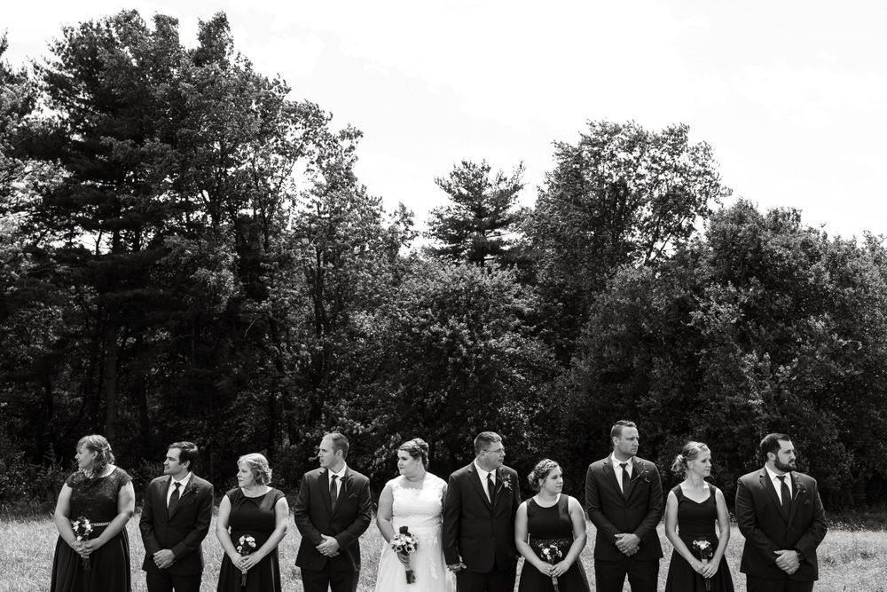 Black and white photo of wedding party arranged in formal line against tree backdrop.