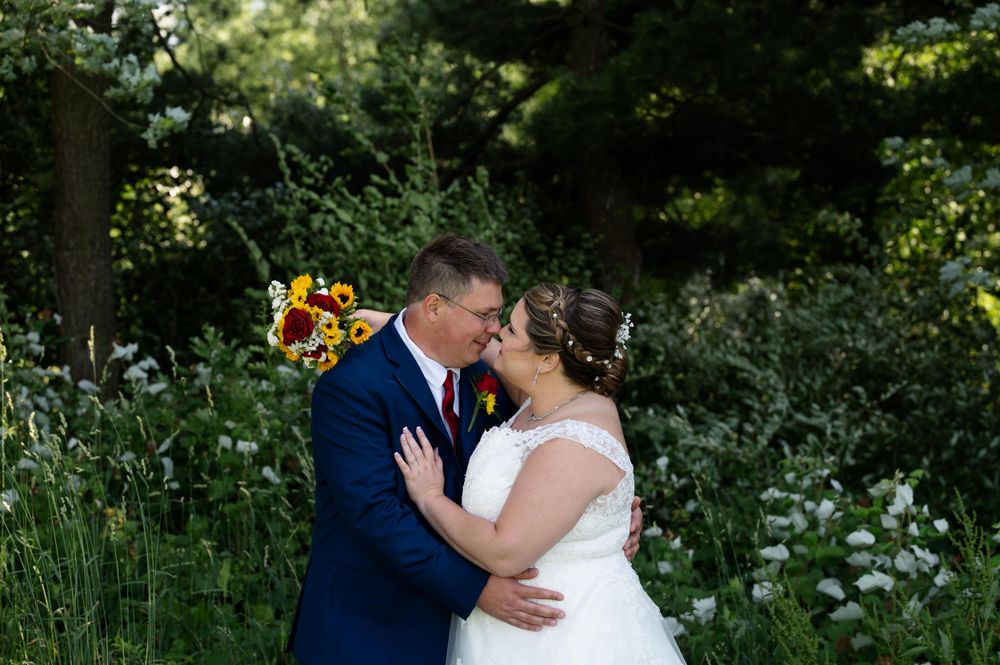 Intimate wedding couple moment captured in lush garden setting with sunflower bouquet.