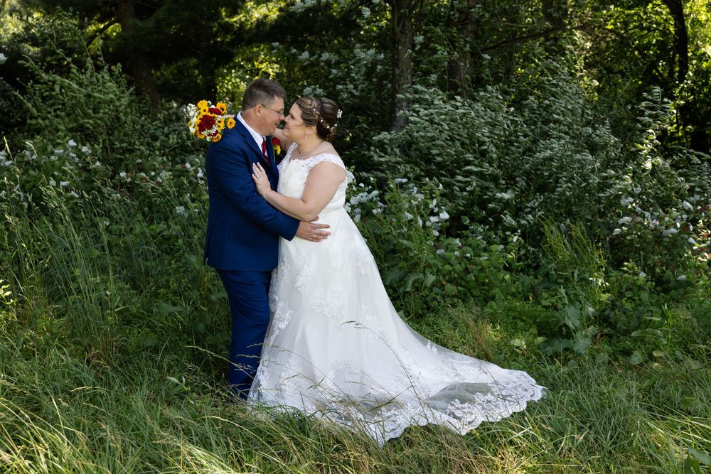 Romantic wedding couple embraces in outdoor garden setting with trailing lace gown.