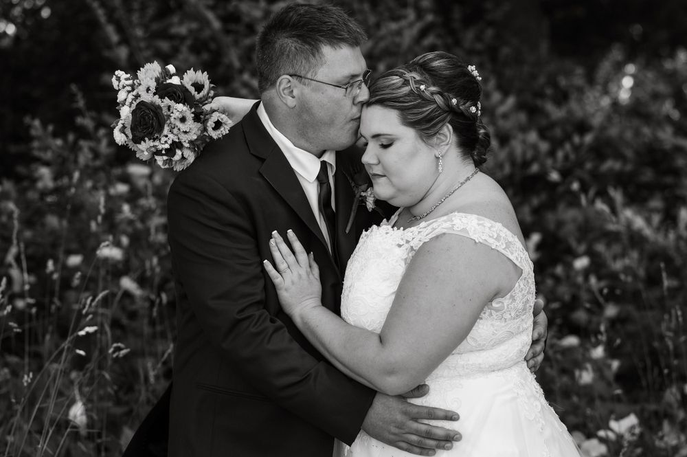 Black and white portrait of tender wedding moment in garden setting.