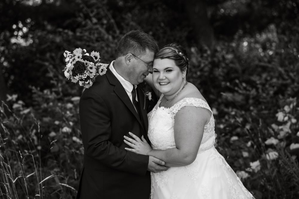 Black and white intimate portrait of wedding couple against foliage backdrop.