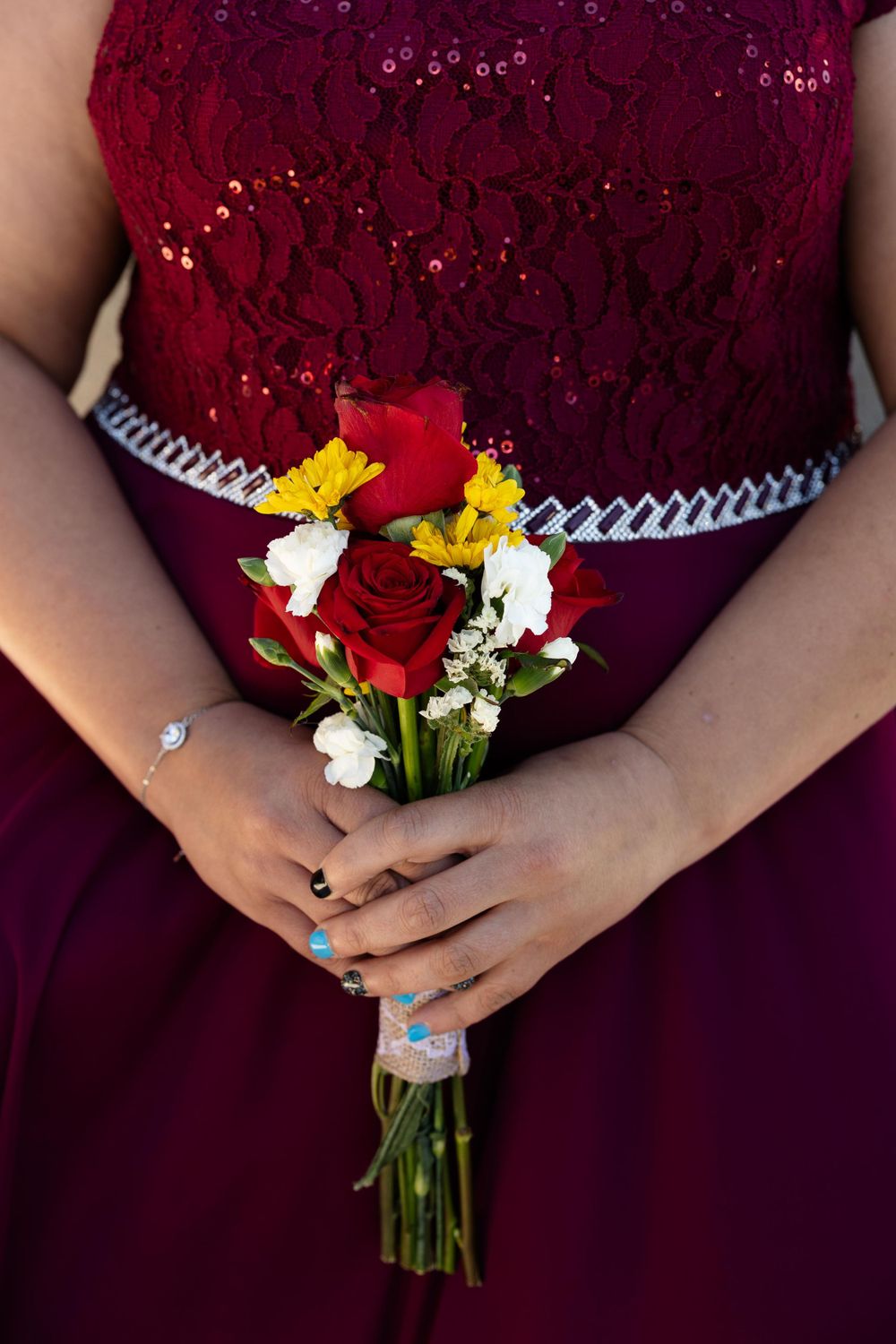Close up of burgundy lace dress with small red and yellow floral bouquet.