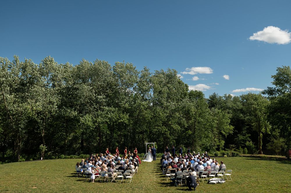 Aerial view of outdoor wedding ceremony with white chairs arranged in rows among trees.