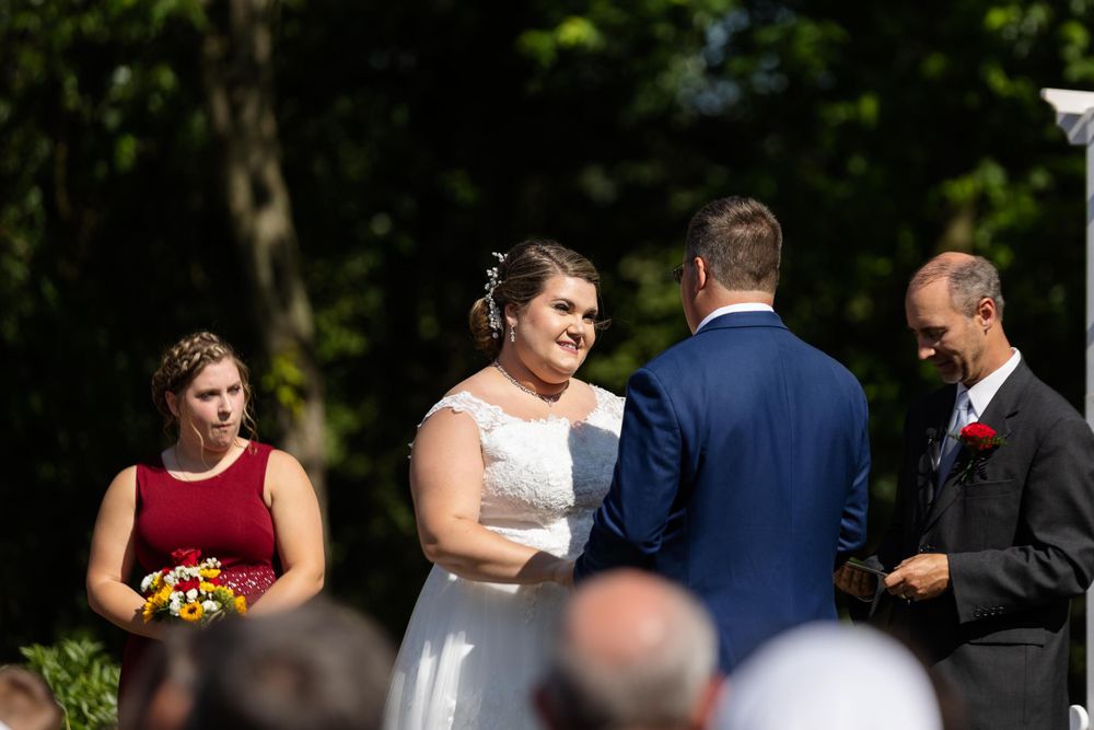 Intimate moment during outdoor wedding ceremony with attendants in navy and burgundy attire.